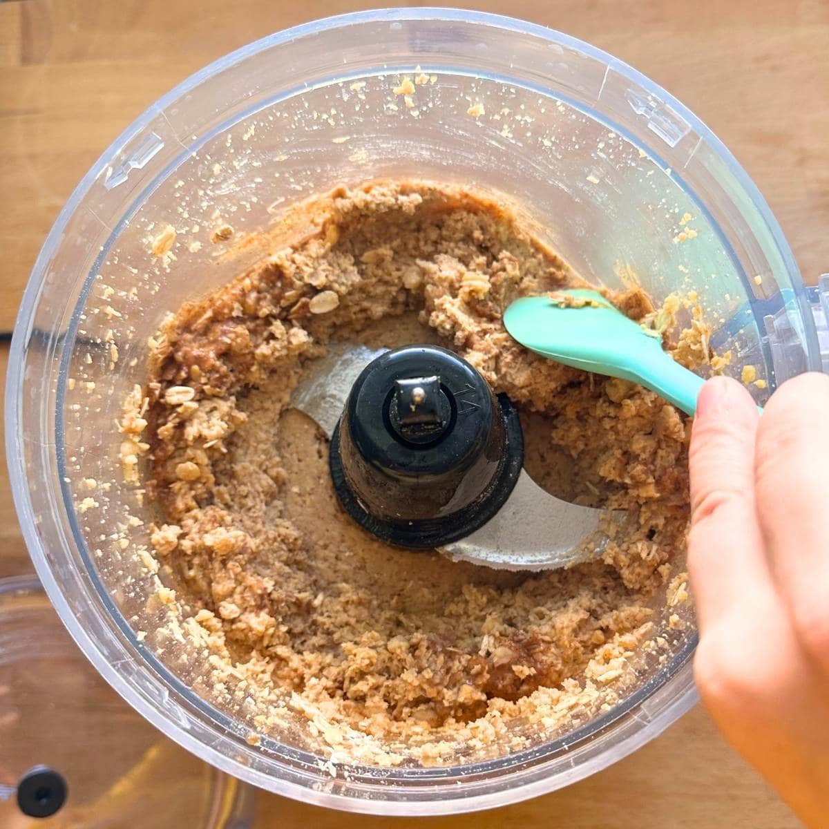 Chickpea cookie dough partially processed, using a spatula to scrap down the sides of the food processor.