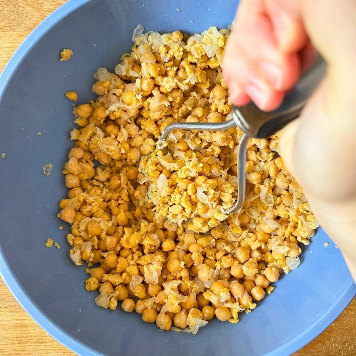 Mashing chickpeas in a bowl with a potato masher.