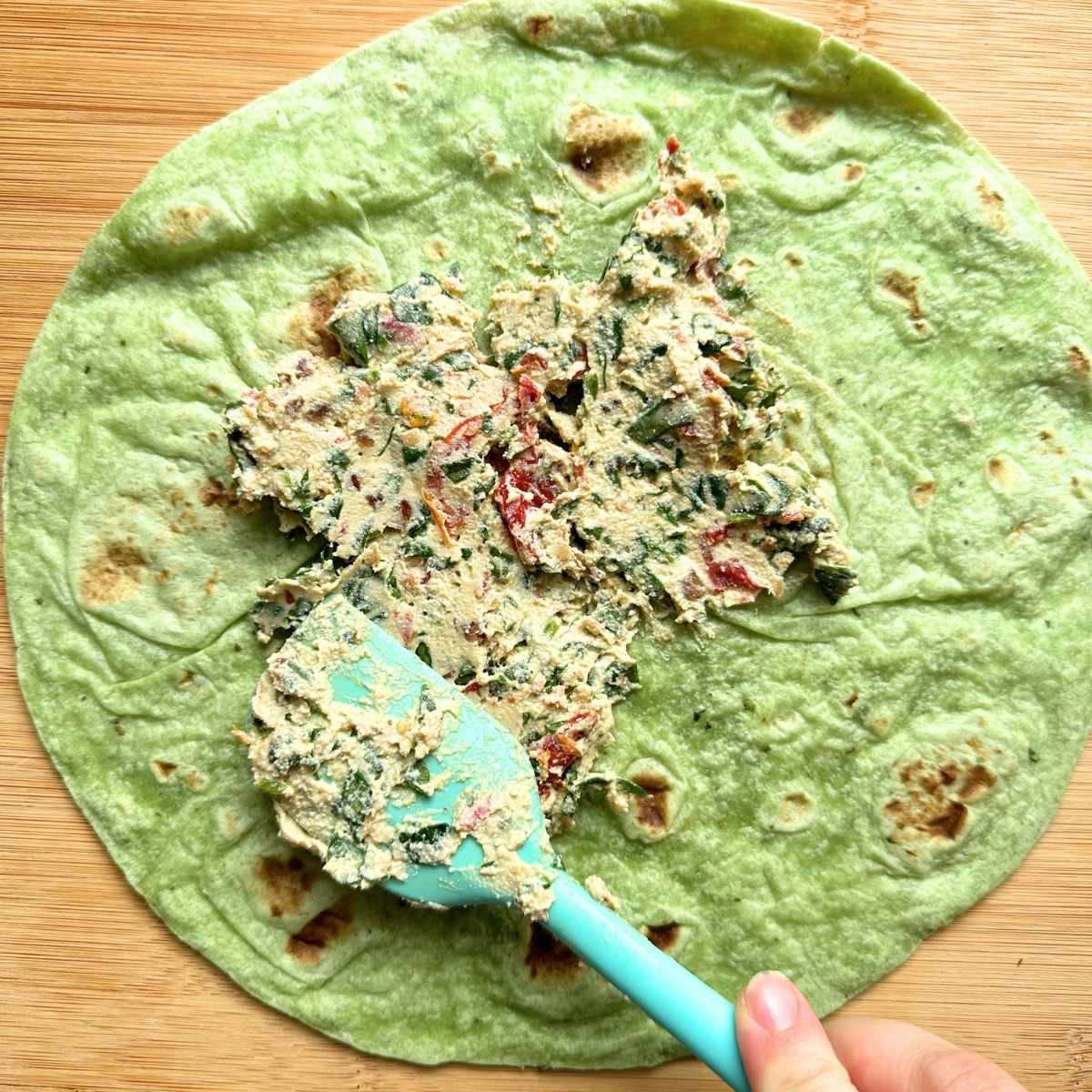 Spreading tofu filling over a green spinach tortilla.