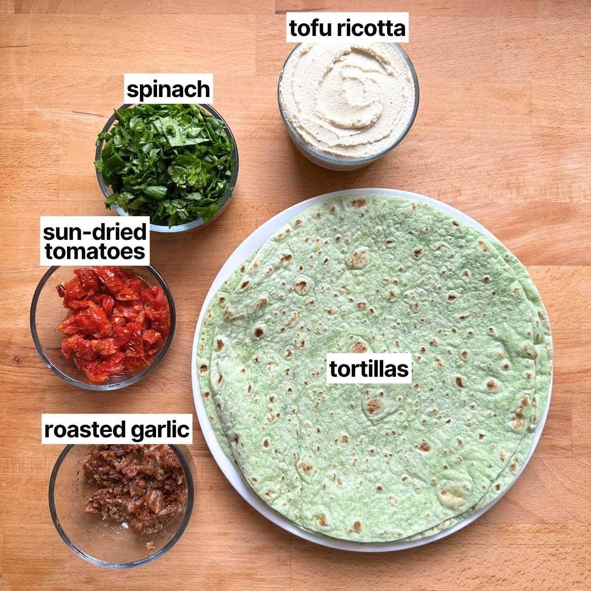 Ingredients needed to make vegan pinwheels: tofu ricotta, spinach, sun-dried tomatoes, roasted garlic, and tortillas.