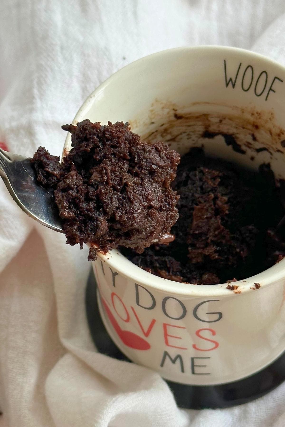 Fork with chocolate zucchini mug cake on it coming out of a mug filled with chocolate zucchini cake.