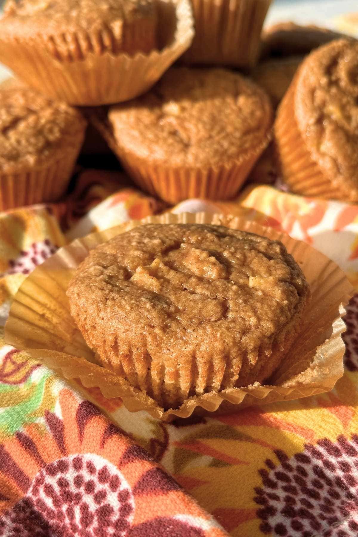 Vegan 3 ingredient apple muffin on top of a muffin liner with more fluffy muffins in the background.