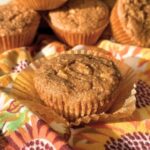 Vegan 3 ingredient apple muffin on top of a muffin liner with more fluffy muffins in the background.
