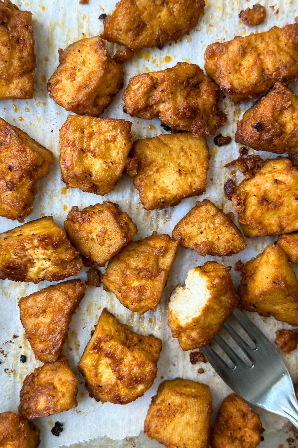 Crispy baked BBQ tofu nuggets on a sheet pan with a fork in one nugget with a bite taken out of it.