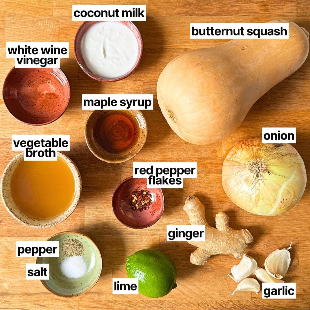 Ingredients needed to make butternut squash soup with labels: white wine vinegar, coconut milk, butternut squash, vegetable broth, maple syrup, red pepper flakes, onion, pepper, salt, lime, ginger, and garlic.