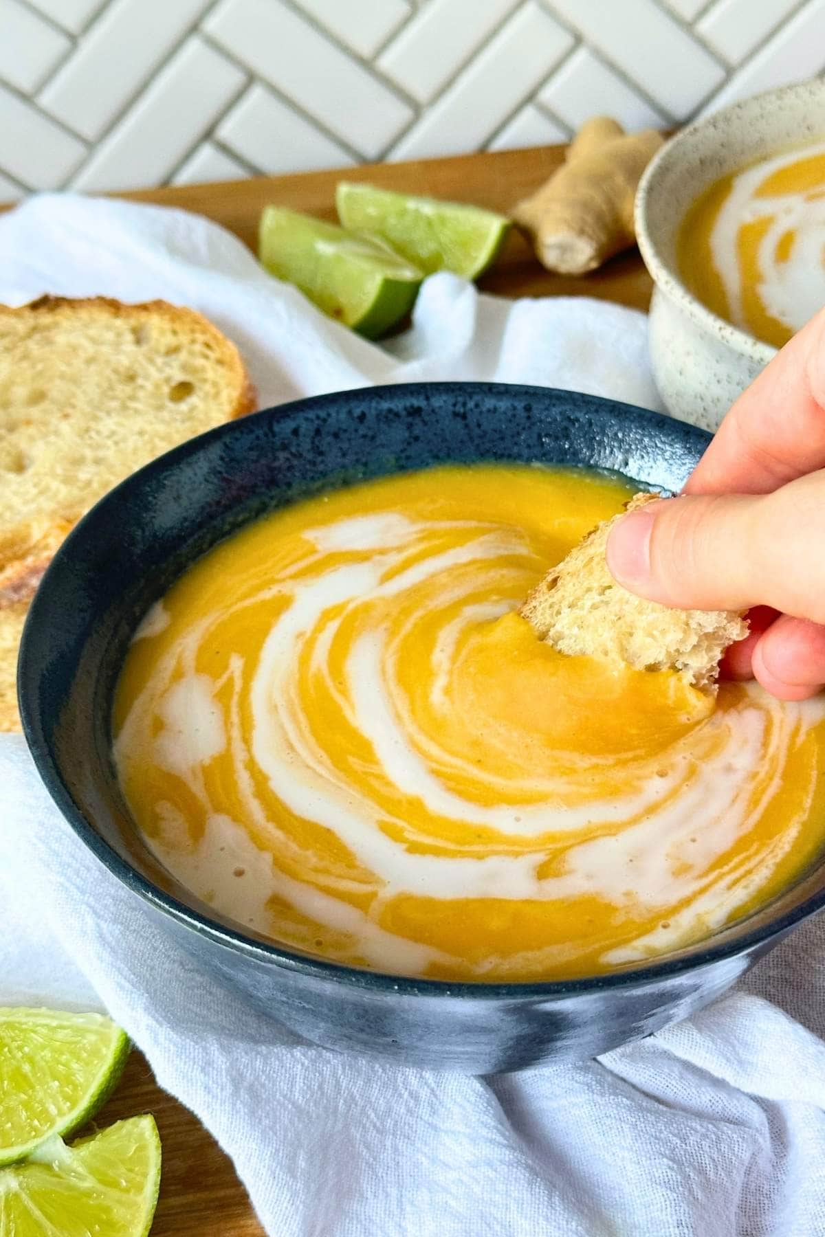 Dunking a piece of sourdough bread into vegan butternut squash soup with coconut milk and ginger.