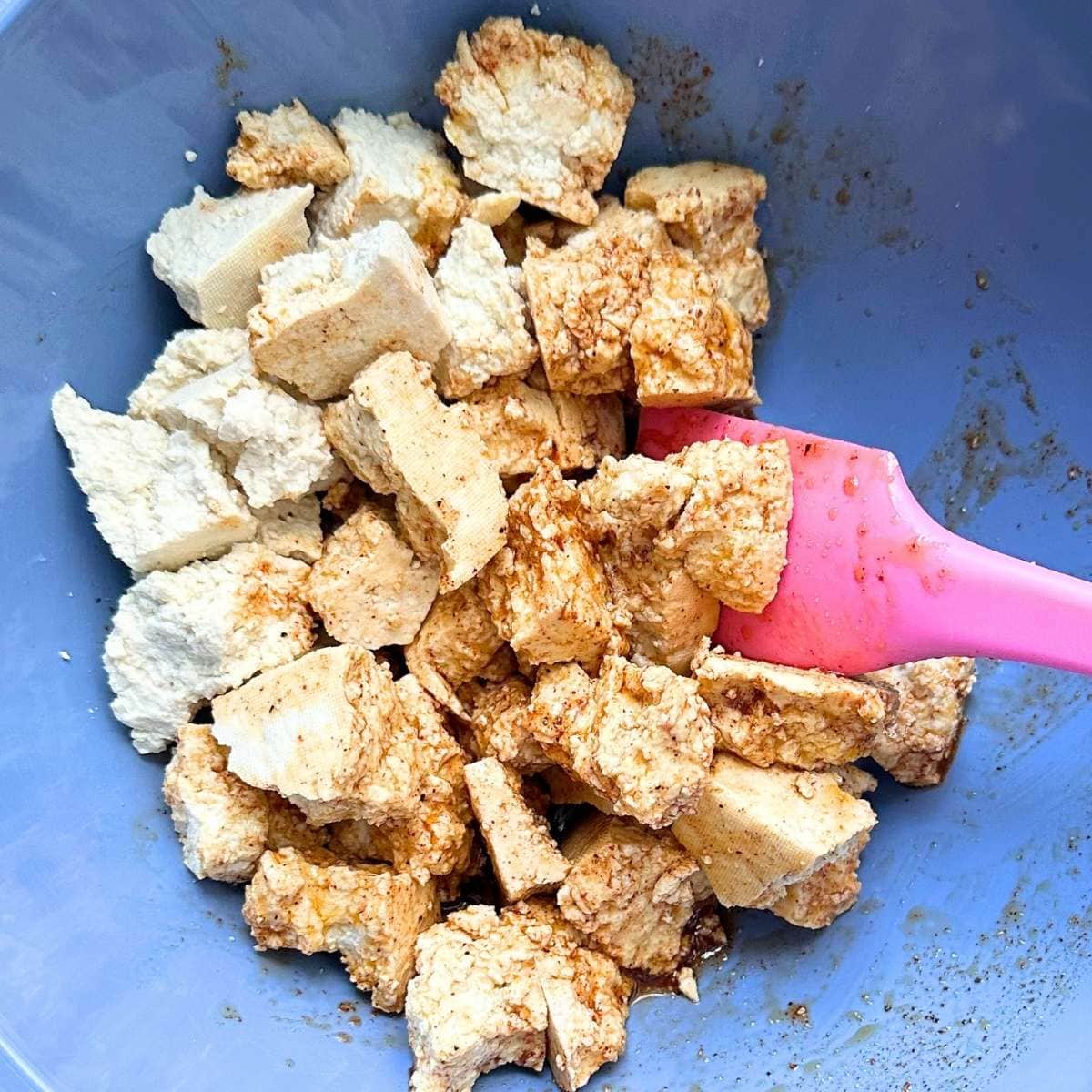 Coating tofu pieces with homemade BBQ sauce in a large bowl.