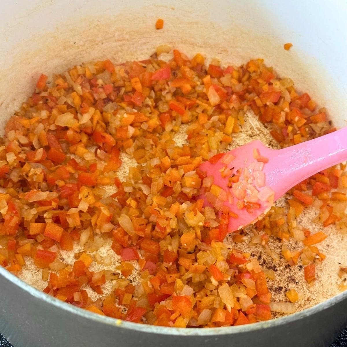 Cooking carrots, peppers, and onion in a large pot with some browned spots on the bottom.