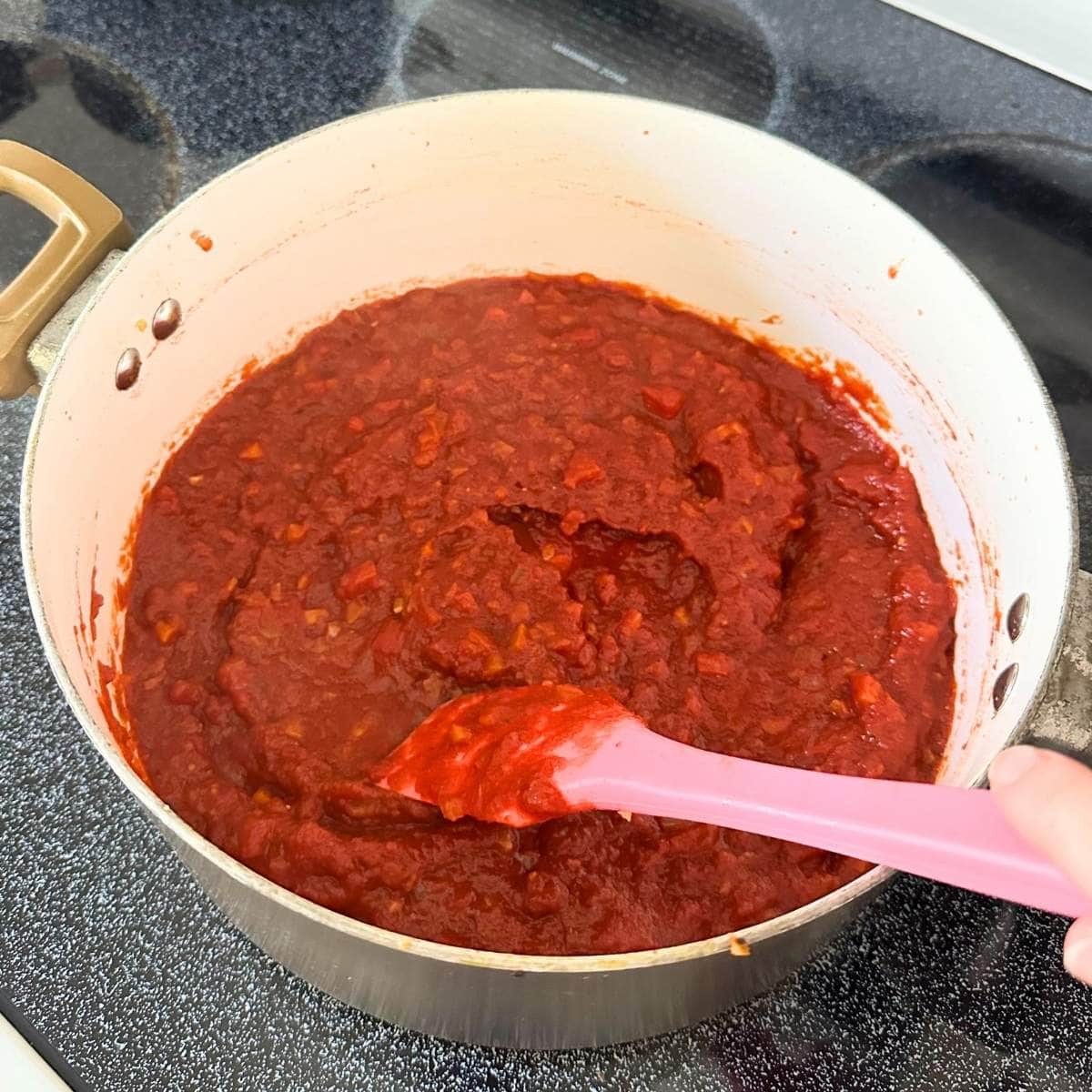 Mixing tomato sauce with cooked carrot, pepper, and onion in a large pot with a spatula.
