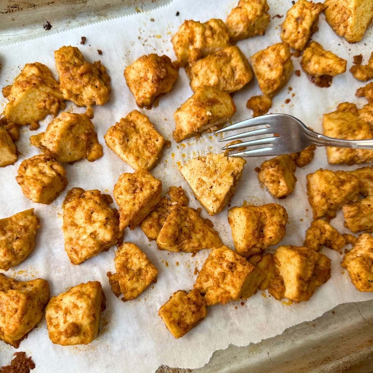 Using a fork to flip baked BBQ tofu halfway through cooking.