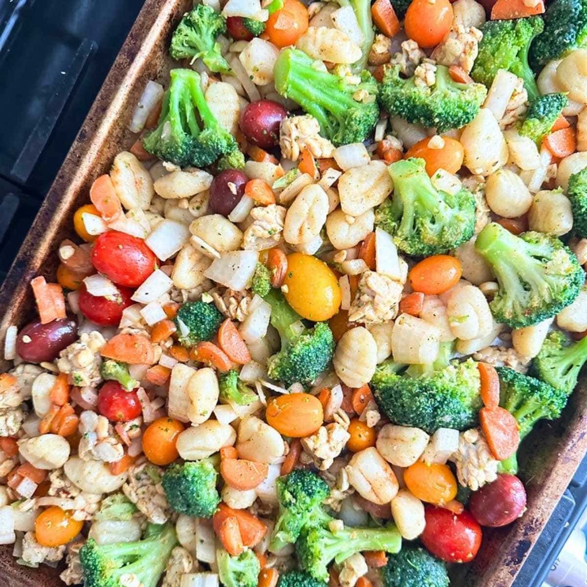 Uncooked sheet pan gnocchi with broccoli, carrots, tomatoes, and tempeh on a pan.