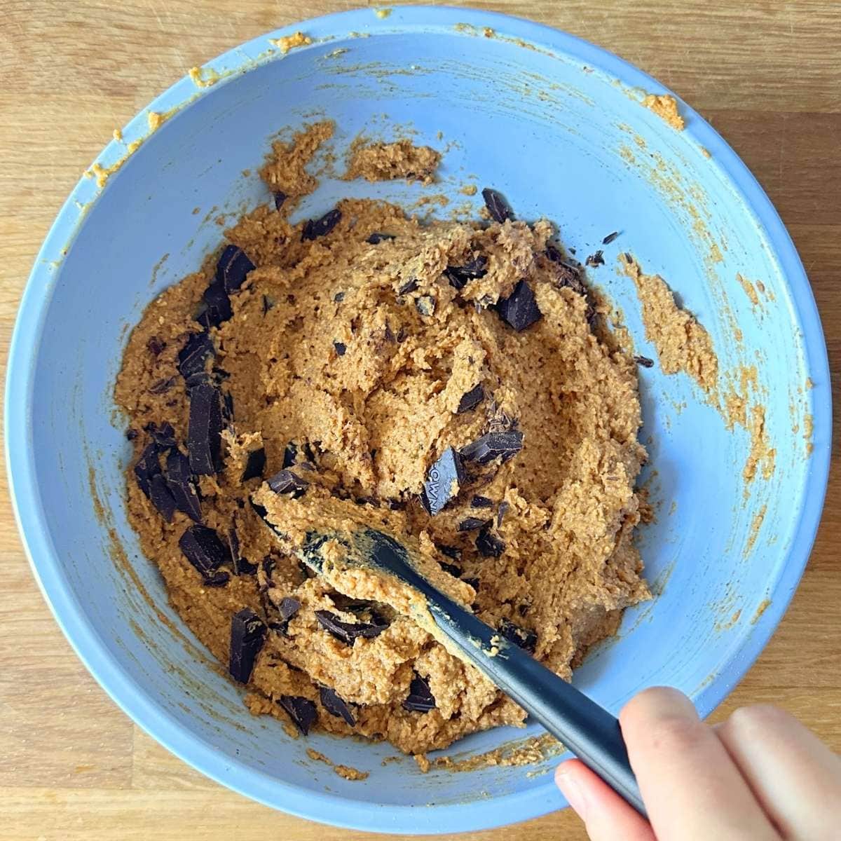 Combining chopped chocolate with the pumpkin chickpea blondie batter in a bowl.