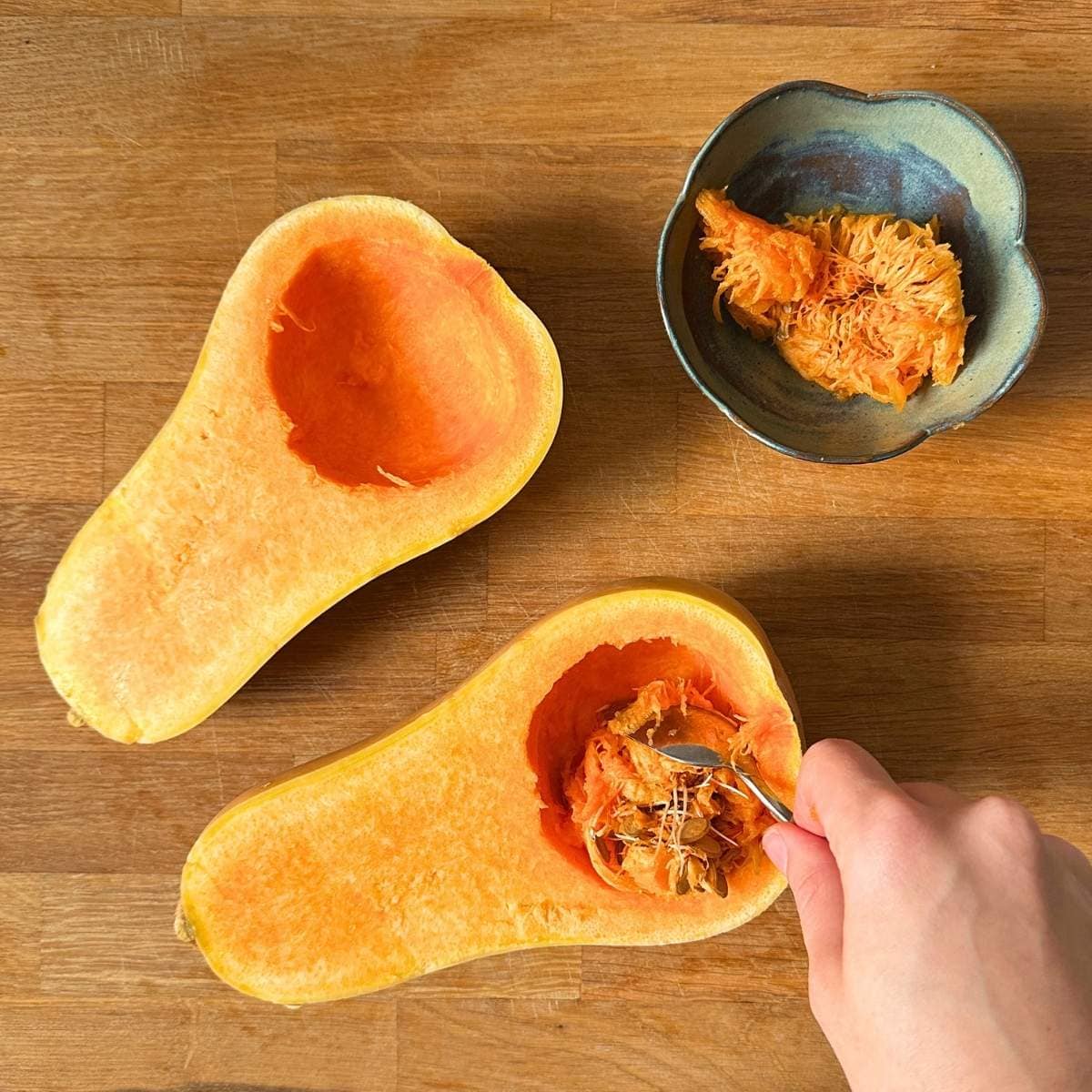 Butternut squash cut in half and scooping out the flesh and seeds with a spoon.