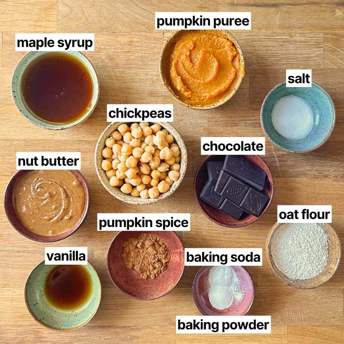 Ingredients needed to make pumpkin chickpea blondies with labels: maple syrup, pumpkin puree, nut butter, chickpea, chocolate, salt, vanilla, pumpkin spice, baking soda, baking powder, and oat flour.