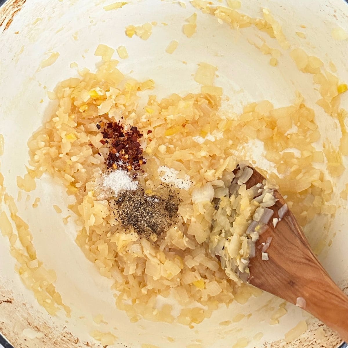 Onion, garlic, and ginger cooked in a pot with salt, pepper, and red pepper flakes sprinkled on top.