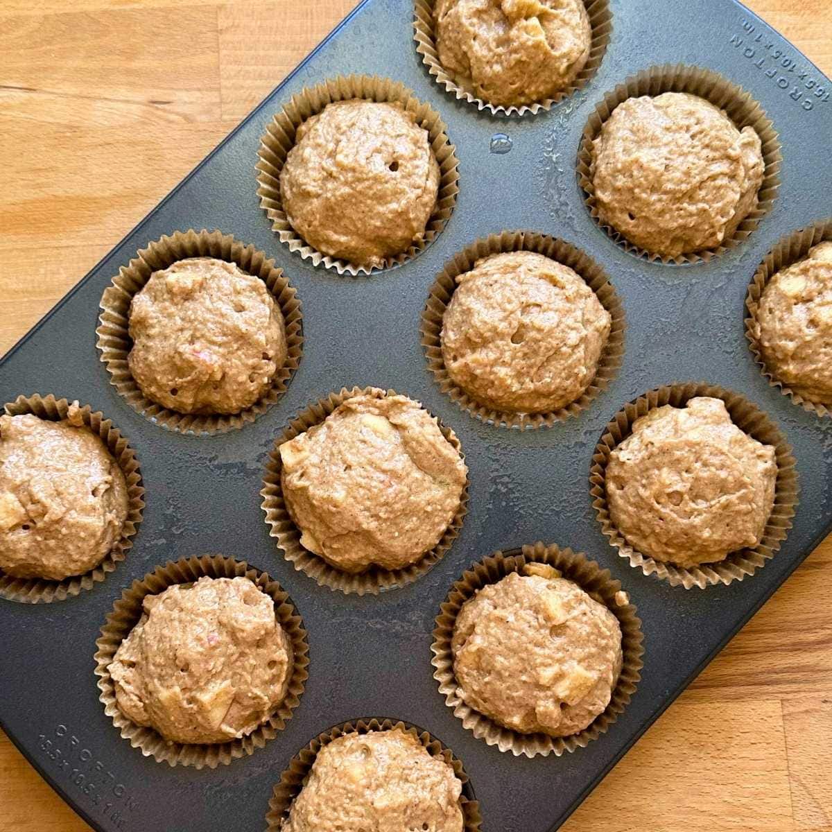 Use a scooper to scoop apple muffin batter into muffin tin lined with muffin liners.