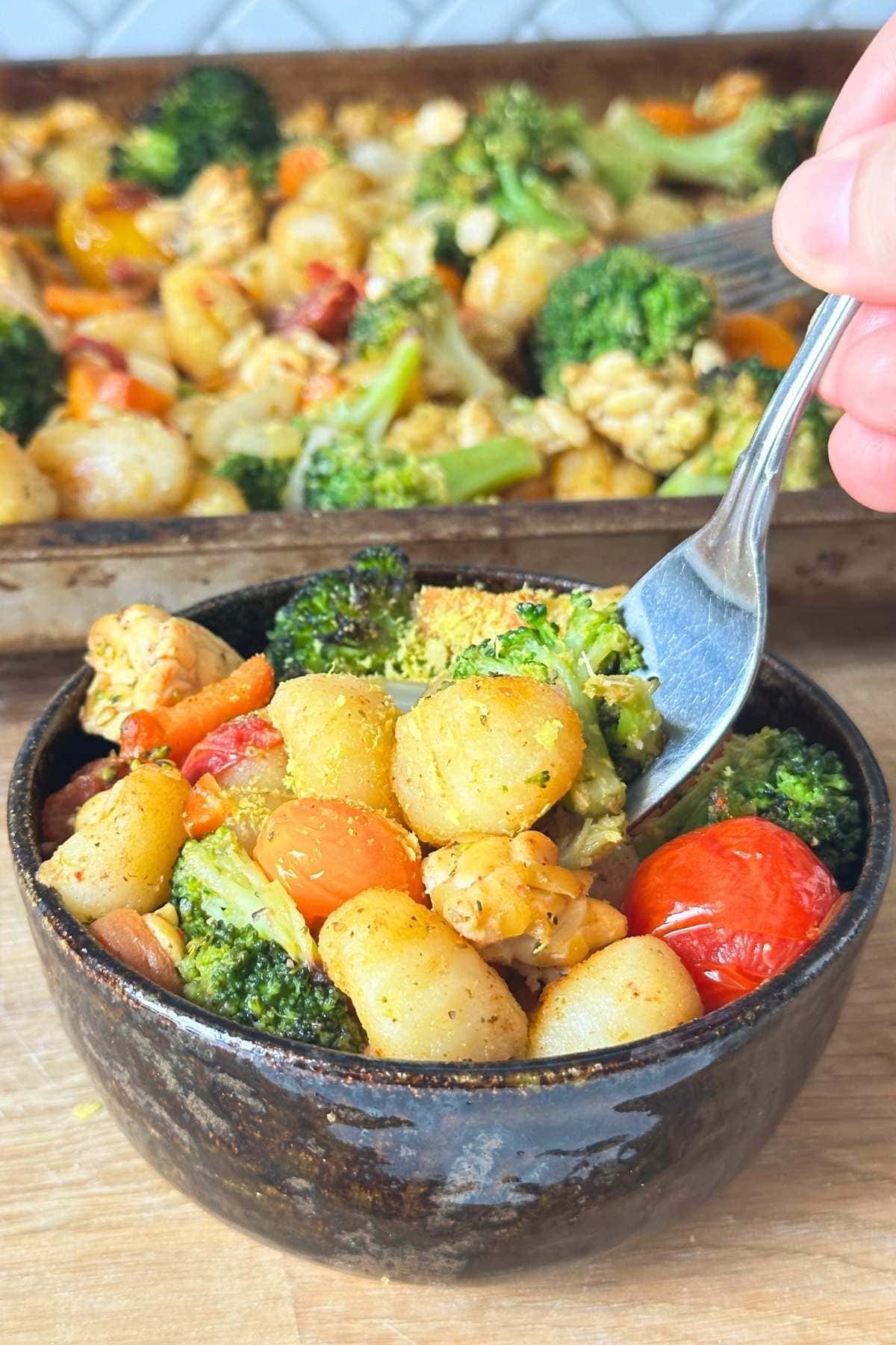 Gnocchi with tomatoes, broccoli, and tempeh in a bowl with nutritional yeast sprinkled on top and a fork grabbing out a bite.