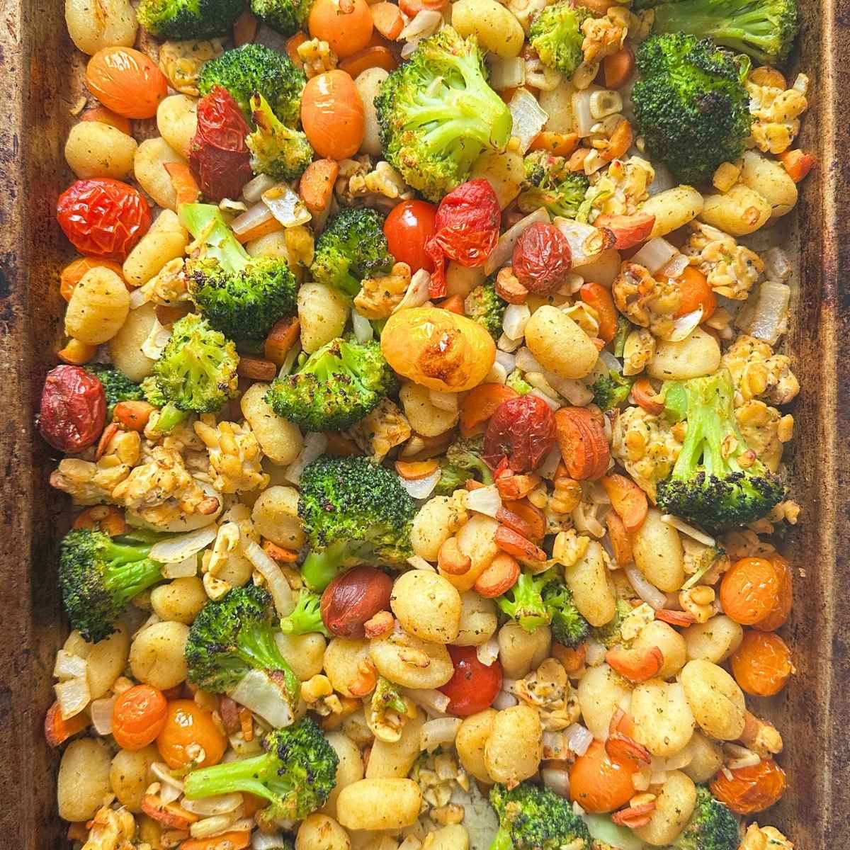 Sheet pan gnocchi with broccoli, carrots, tomatoes, and tempeh on a pan.