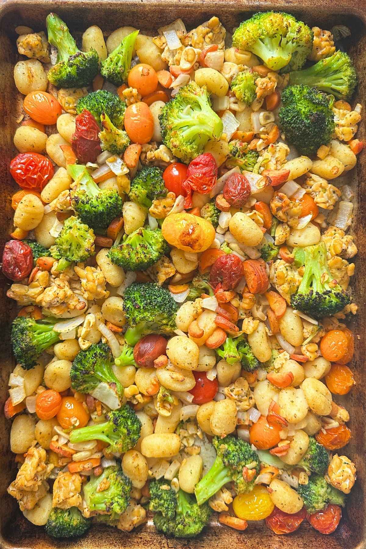 Roasted sheet pan gnocchi with broccoli, carrots, tomatoes, and tempeh on a pan.