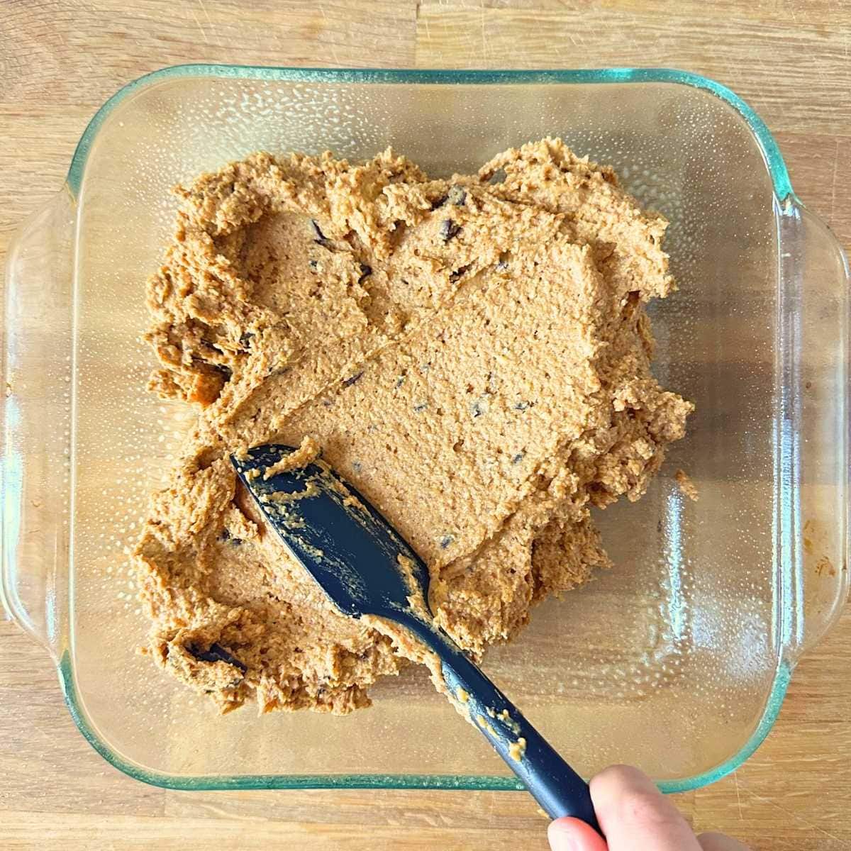 Spreading pumpkin blondie batter in a glass baking pan.
