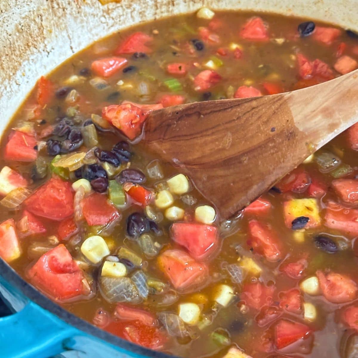 Adding broth, black beans, tomatoes, and corn to soup pot.