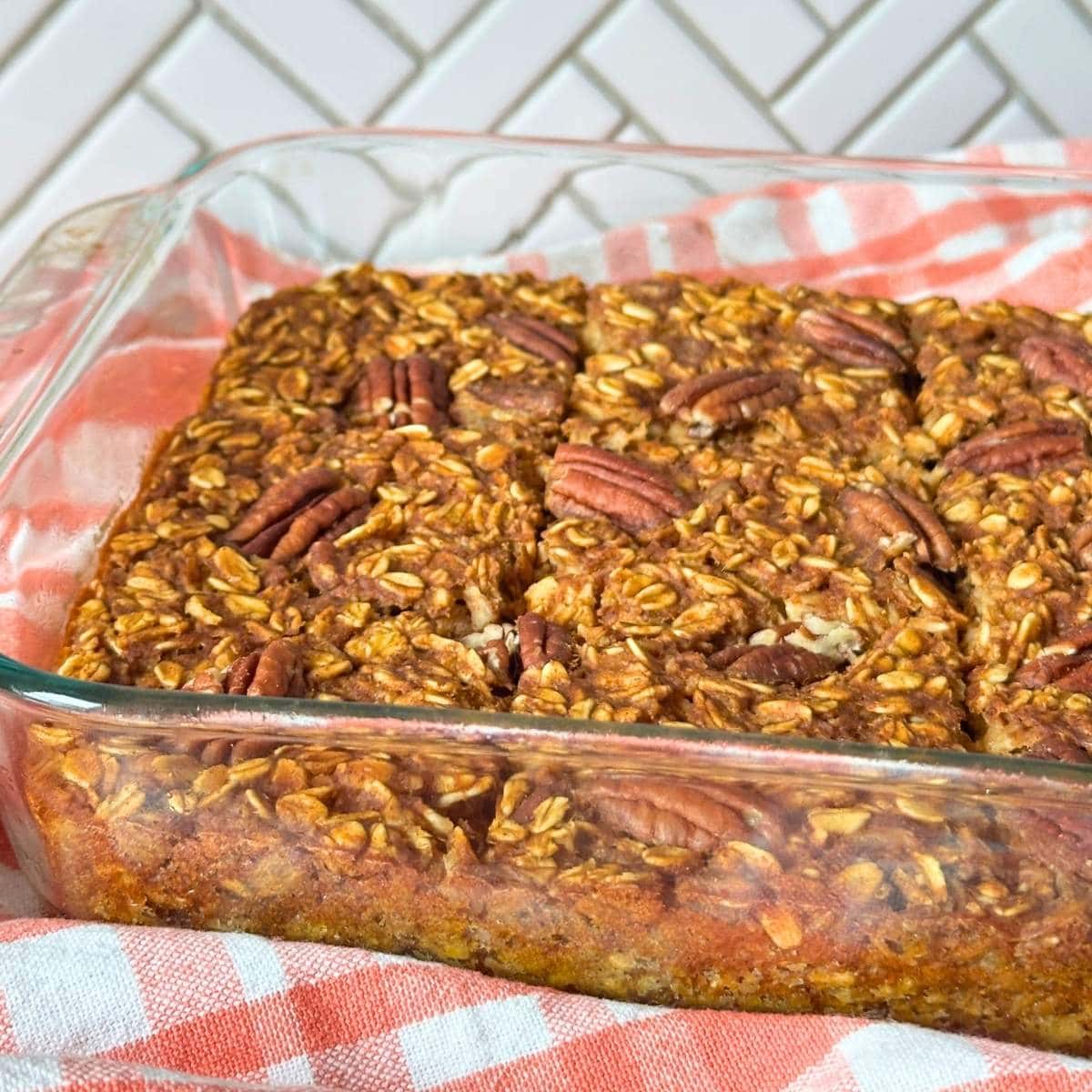Baked pumpkin oatmeal with pecans on top baked and sliced into squares in a glass pan.