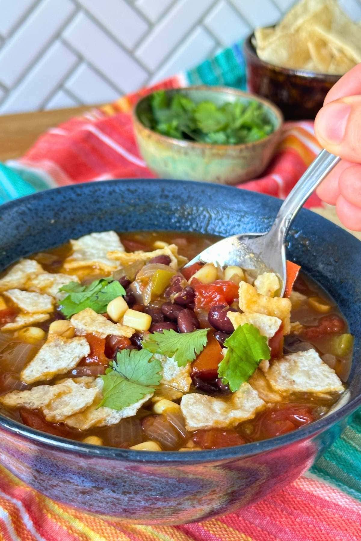 Black bean tortilla soup in a blue bowl topped with cilantro and crushed tortilla chips.