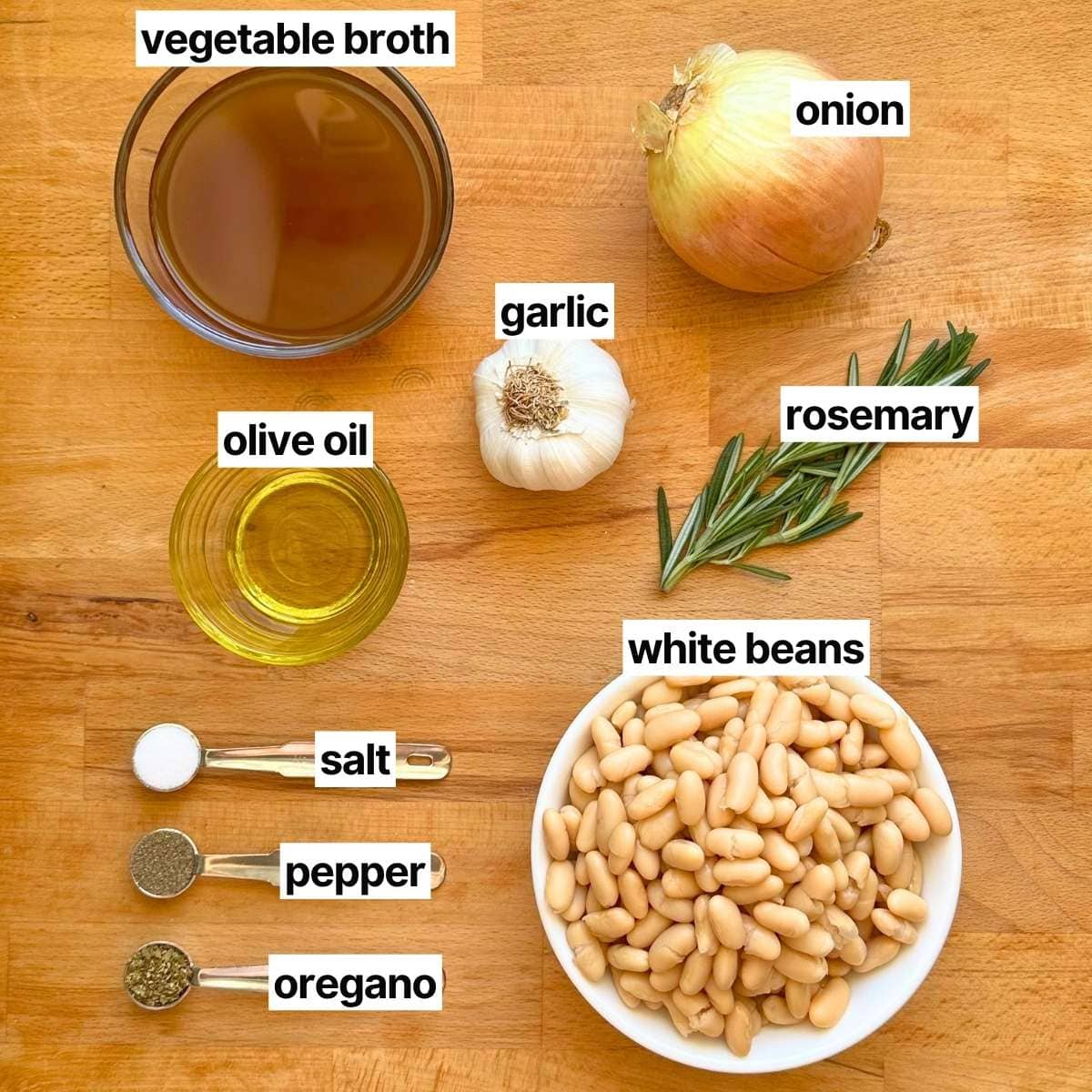 Ingredients needed to make braised white beans with labels: vegetable broth, onion, garlic, olive oil, rosemary, salt, pepper, oregano, and white beans.