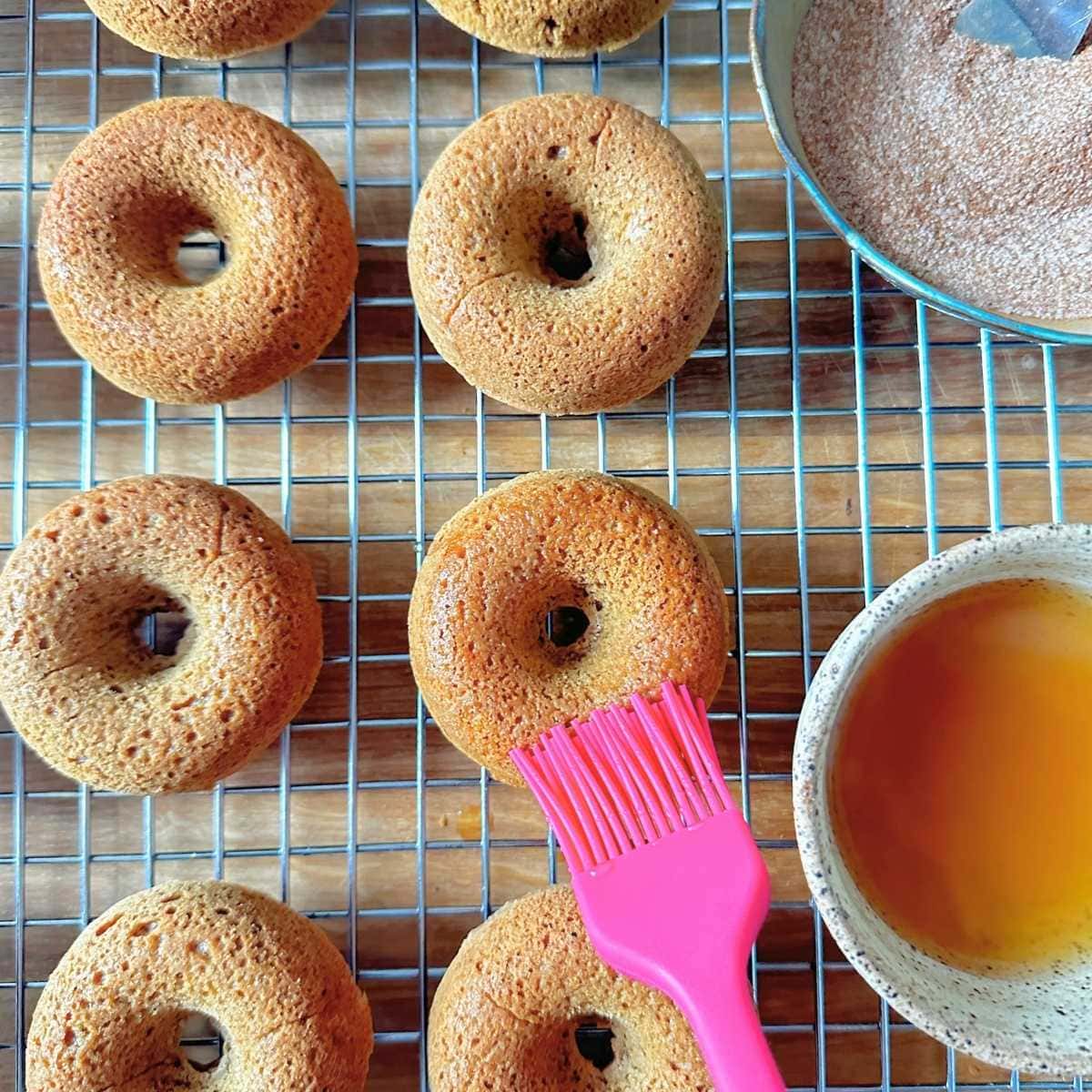Brushing baked apple cider donuts with more apple cider.