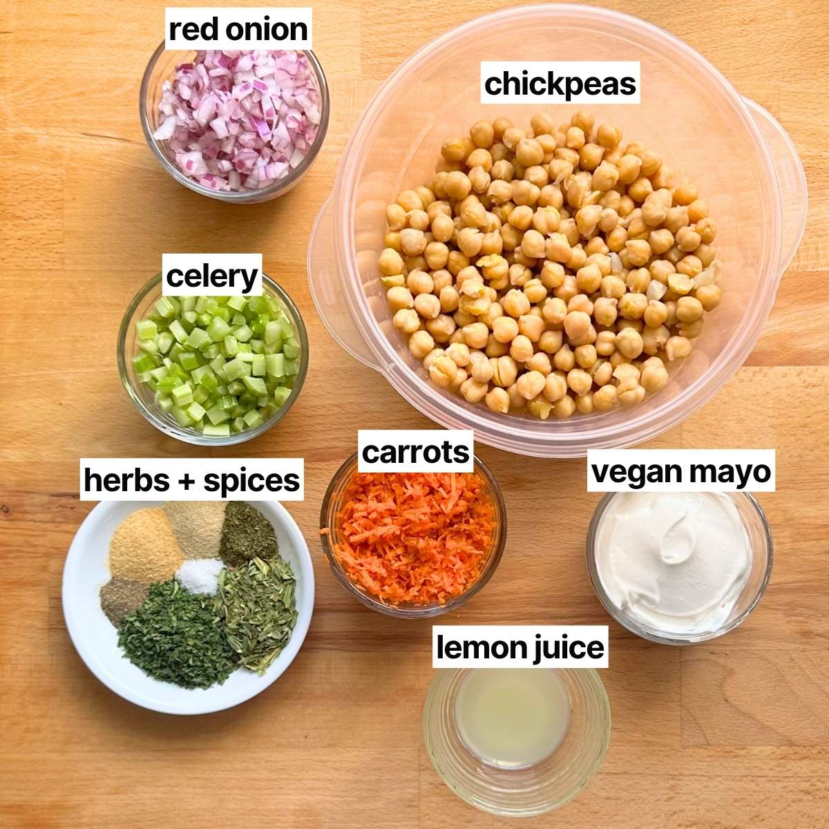 Ingredients to make chickpea chicken salad with corresponding written labels: chickpeas, red onion, celery, carrots, vegan mayo, herbs + spices, and lemon juice.
