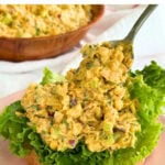 Scooping chickpea chicken salad onto a piece of bread with lettuce using a spoon.