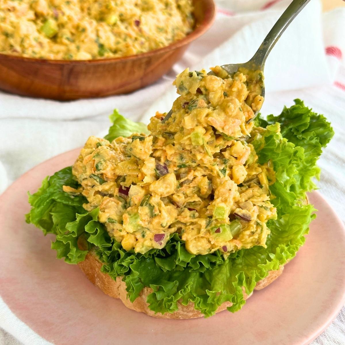 Scooping chickpea salad onto a piece of bread with lettuce using a spoon.