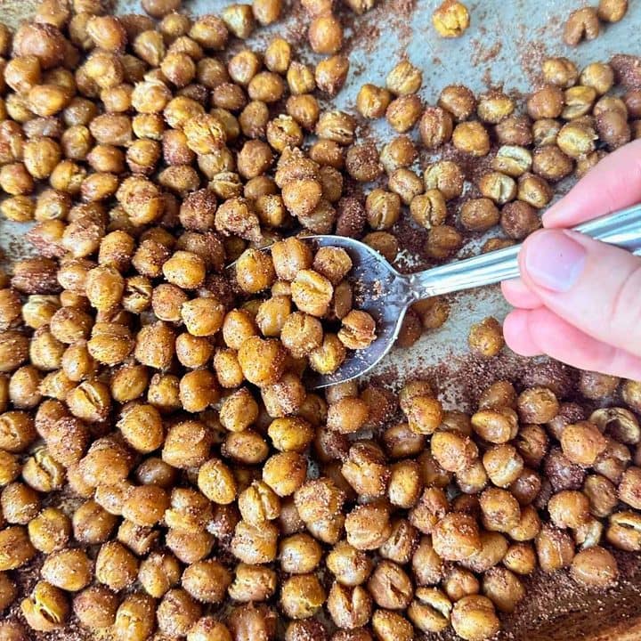 Cinnamon sugar chickpeas on a sheet pan with a large spoon scooping up the crunchy chickpeas coated in cinnamon sugar.