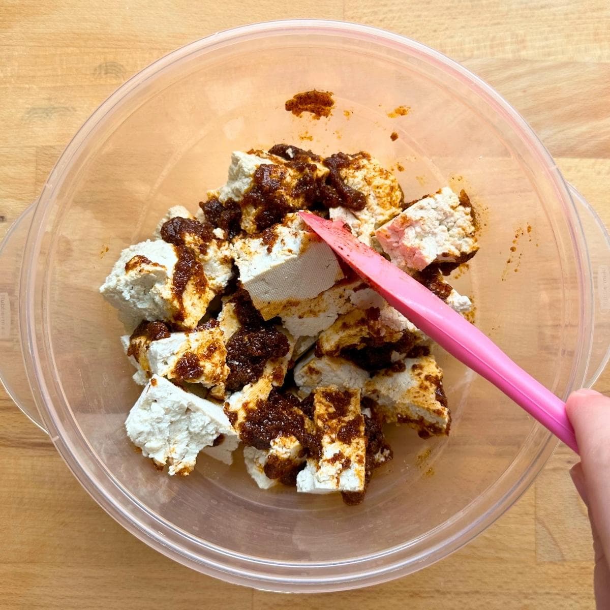 Tossing tofu chunks with wet rub in a large bowl.
