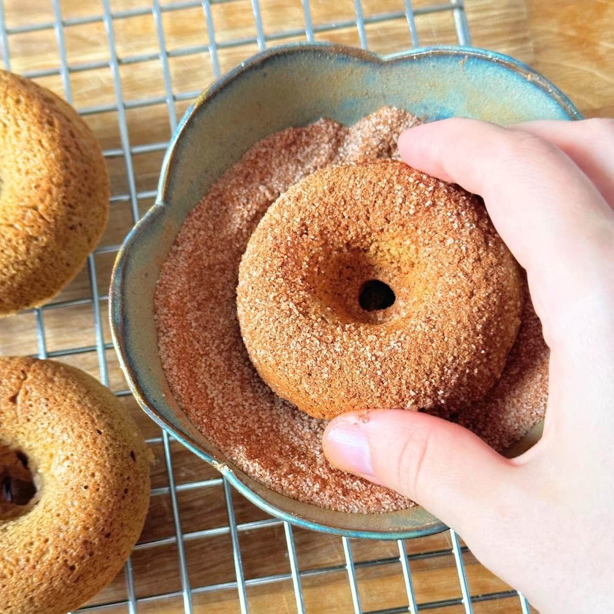 Rolling apple cider donut in a bowl with cinnamon sugar.
