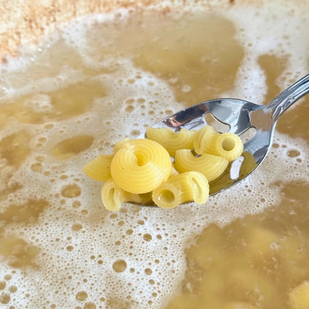 Lifting up cooked macaroni noodles from a pot of boiling water.
