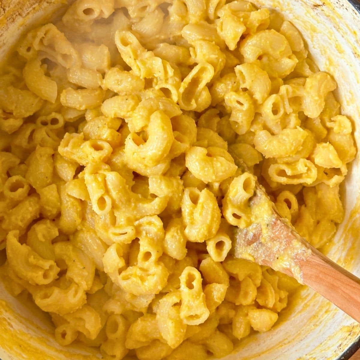 Butternut squash cheese sauce mixed with macaroni noodles in a large pot.