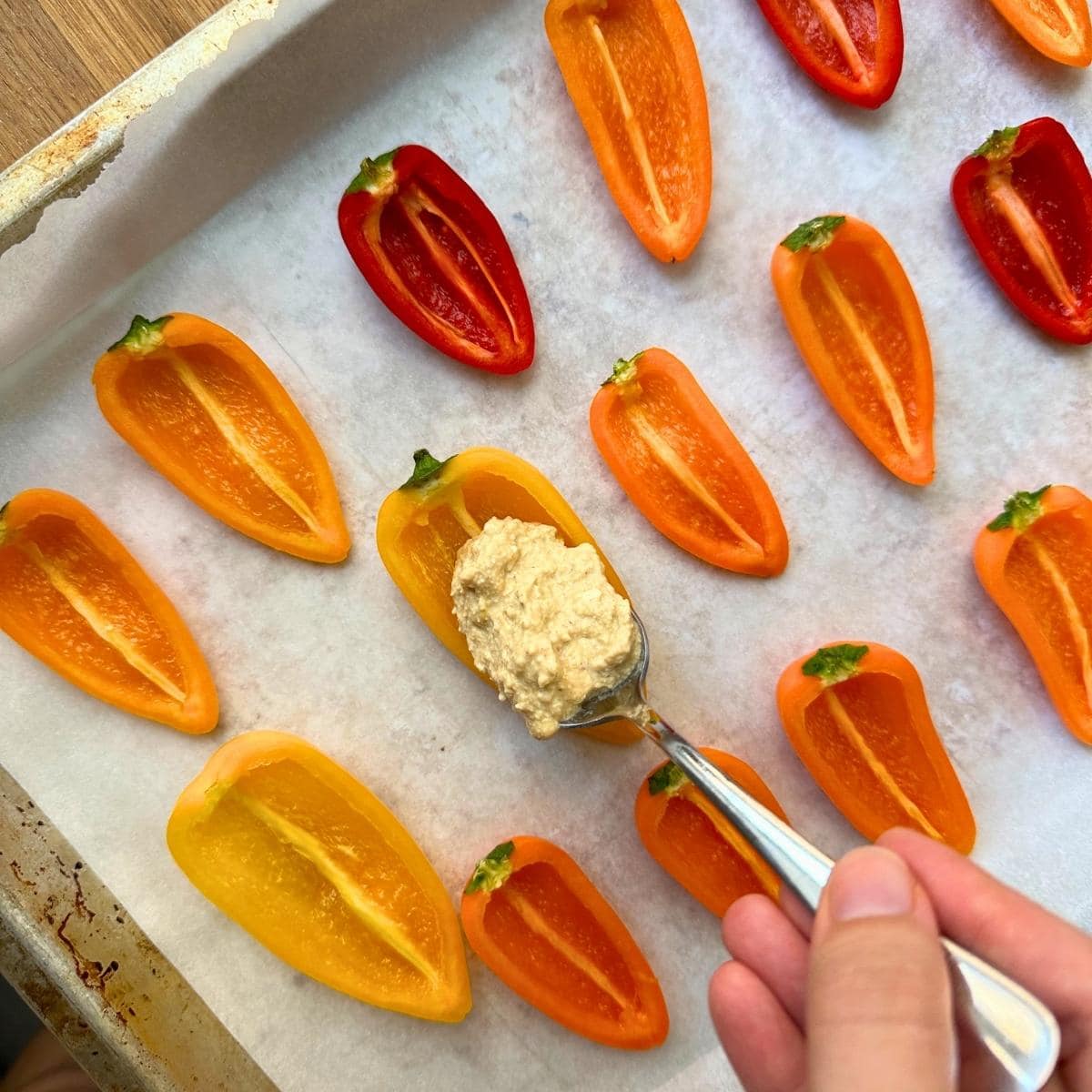 Spooning tofu filing into halved mini peppers using a spoon.