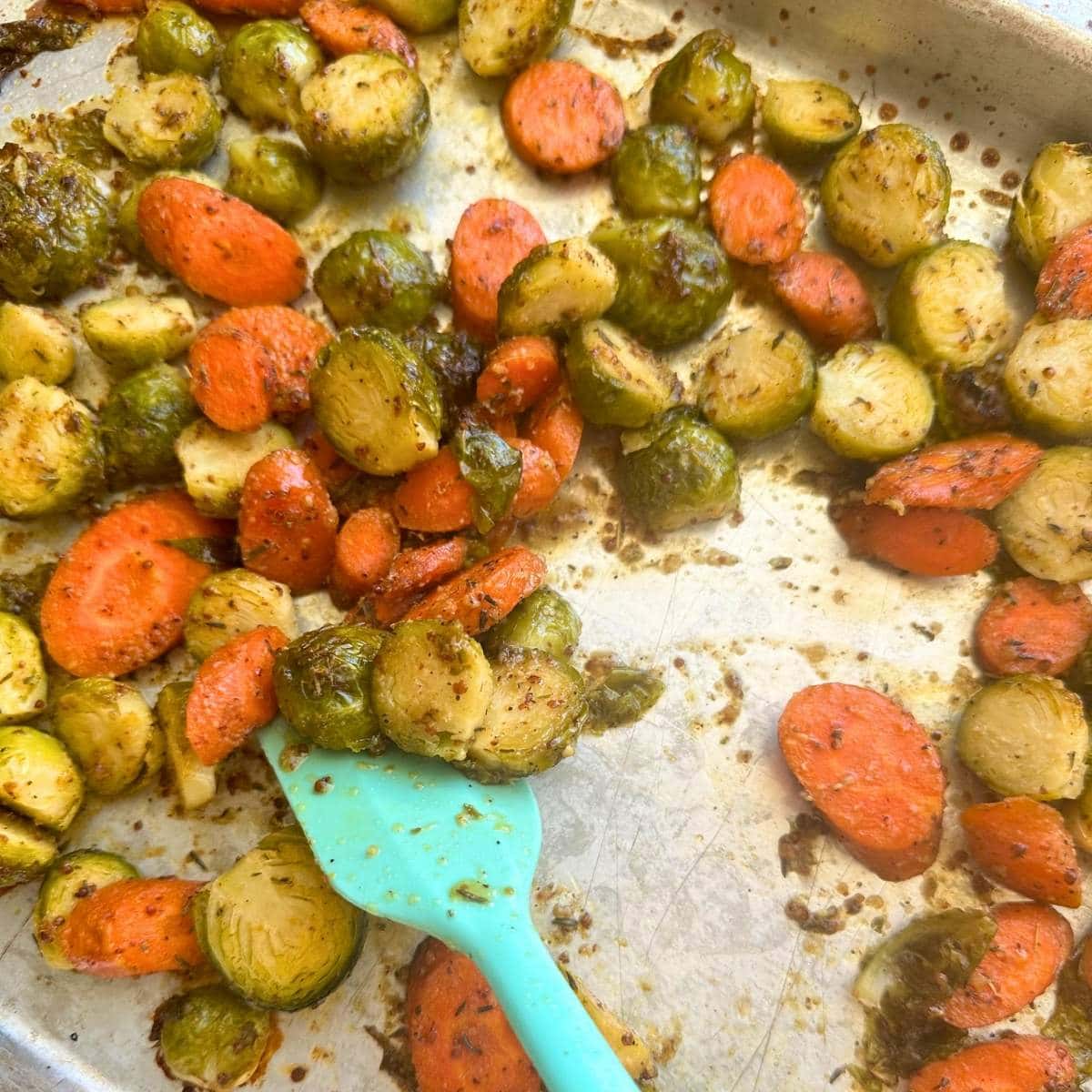Flipping partially cooked Brussels sprouts and carrots on a sheet pan.