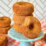 Stack of three vegan gluten-free apple cider donuts on a blue pedestal with another donut with a bite taken out of it resting on the side.