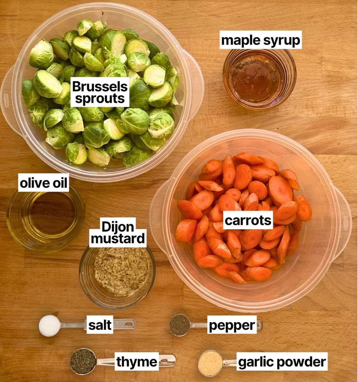 Ingredients to make maple roasted Brussels sprouts with corresponding labels: Brussels sprouts, maple syrup, olive oil, Dijon mustard, carrots, salt, pepper, thyme, and garlic powder.