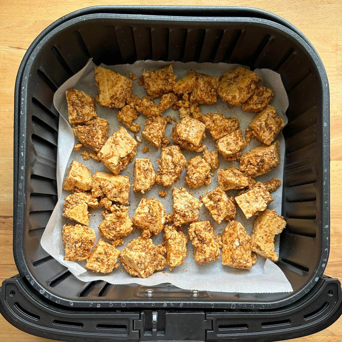 Seasoned tofu bites in an air fryer lined with parchment paper.