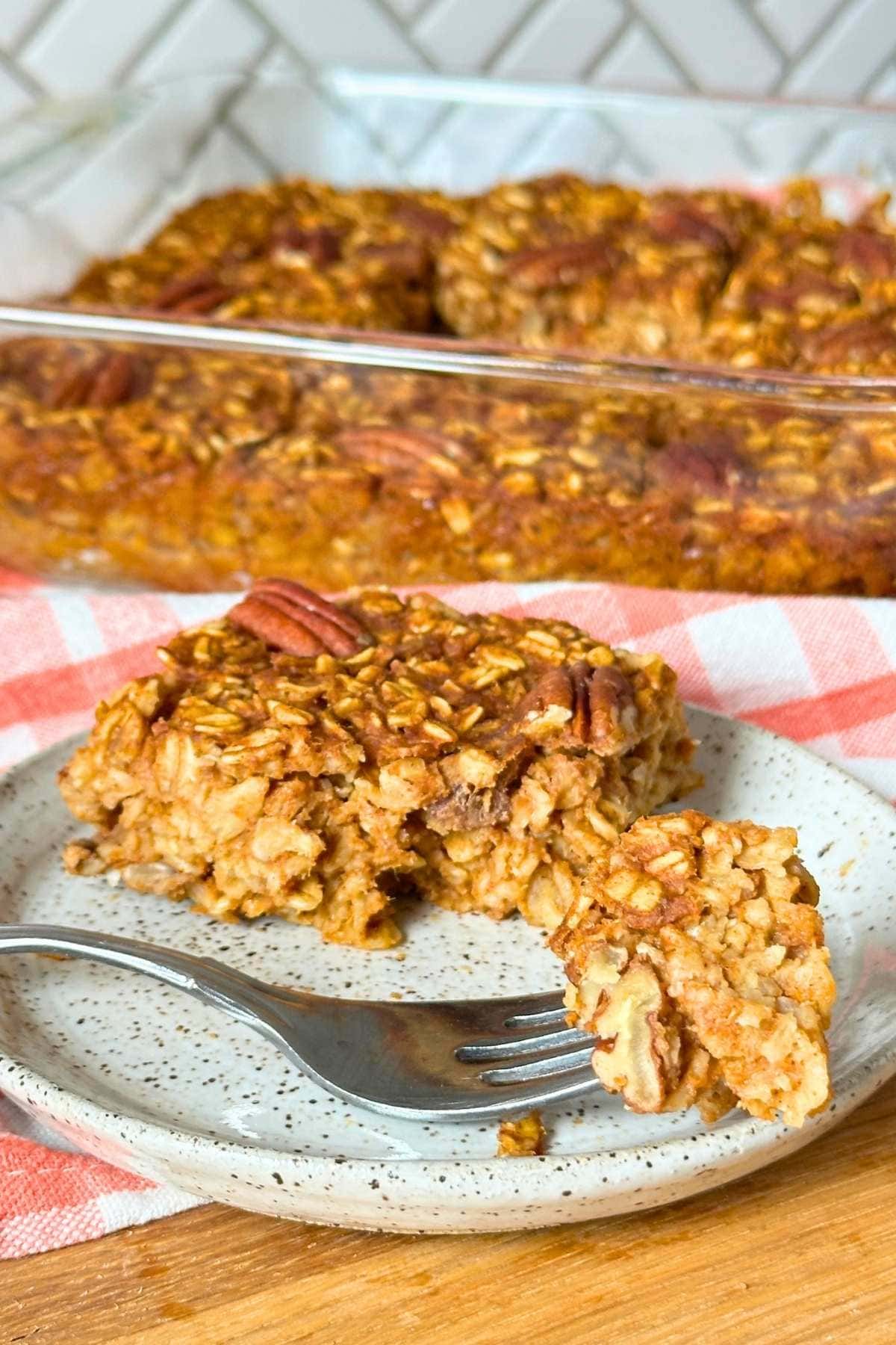 A square of vegan pumpkin baked oatmeal on a plate with a bite taken out on a fork.