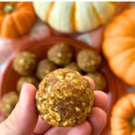 Hand holding a pumpkin spice protein ball with more in the background on a plate.