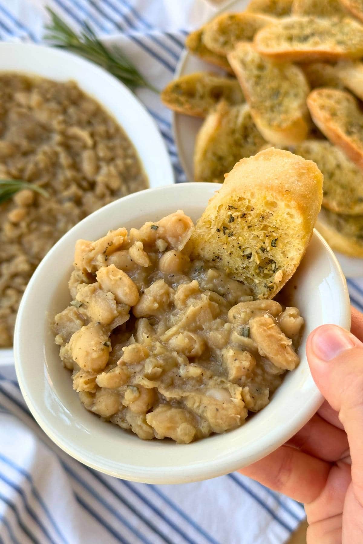 Small bowl filled with creamy braised  white beans and a piece of garlic rosemary crostini.
