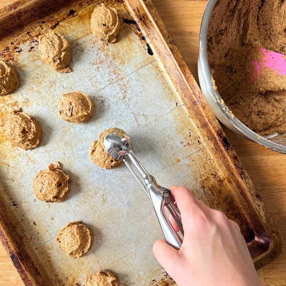 Scooping rested pumpkin cookie dough onto a baking sheet with a tablespoon sized scooper.