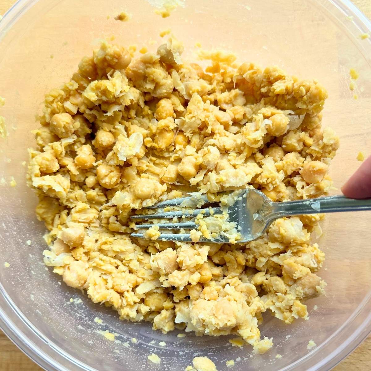Fork smashing chickpeas in a bowl.