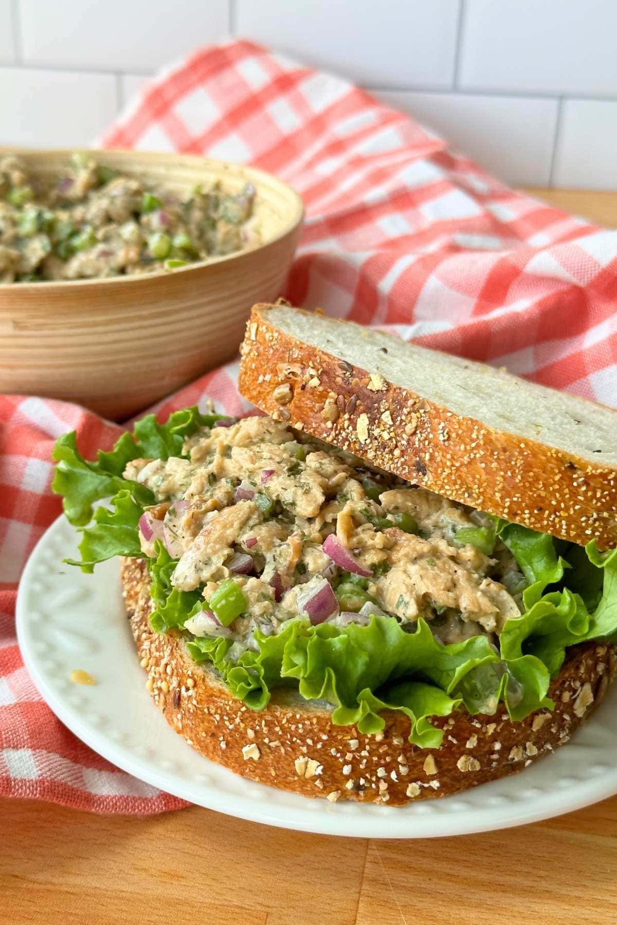 Vegan soy curl chicken salad on a piece of bread with a bed of lettuce, more vegan chicken salad is in the background in a bowl.