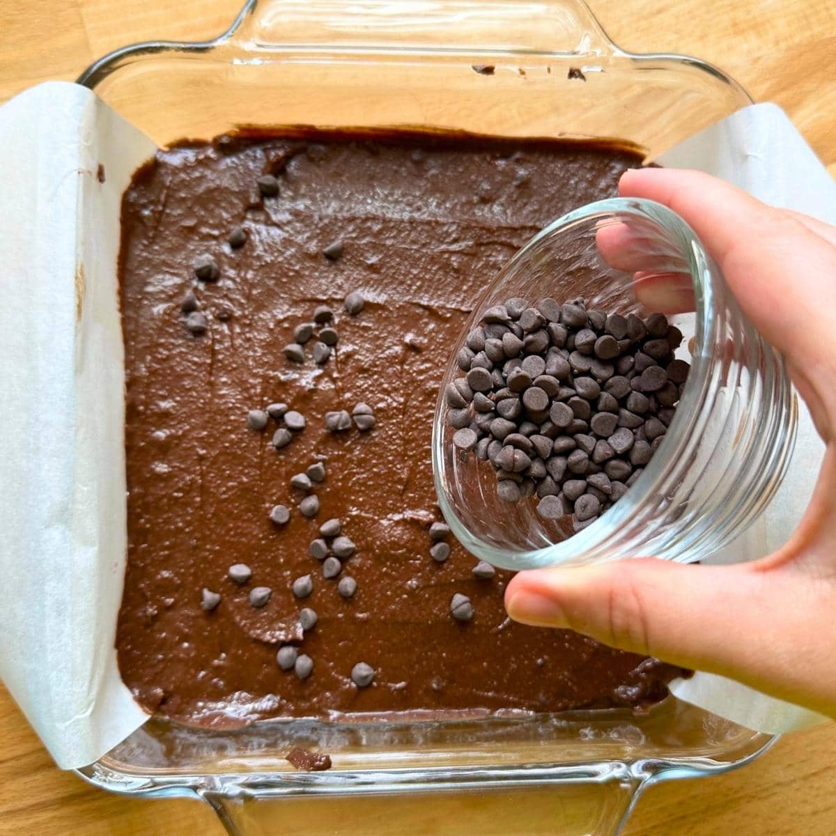 Sprinkling chocolate chips over glass pan filled with chickpea brownie batter.