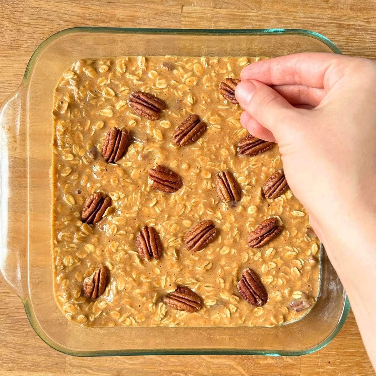 Topping a pan of unbaked pumpkin oats with pecans.